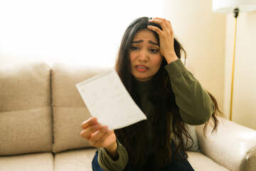 Stressed woman holding an upsetting bill or invoice, feeling anxious about household expenses and...