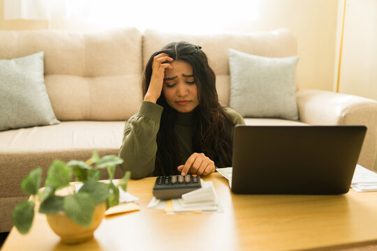 Woman feeling stressed and anxious, calculating bills and taxes with a laptop and calculator, dealing with financial difficulties