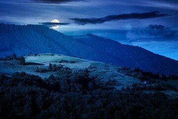 mountainous countryside landscape with rolling hills on summer night. rural area in full moon light. beautiful view of place with grassy pastures. background for fake news or conspiracy concepts