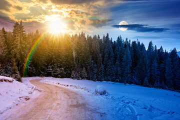 winter solstice landscape with snow covered country road winding through forest in mountains. day and night time change concept. alpine countryside with sun and moon. duality and transition template