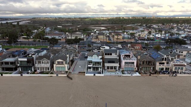 Overhead aerial shot of beachfront houses in Newport Beach on a cloudy, rainy day. The Orange County coastline appears quiet and atmospheric with subdued ocean tones and minimal activity