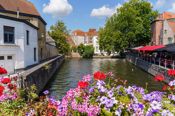 A street with a canal and a row of buildings in Bruges Belgium. The canal is lined with flowers and...
