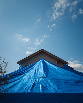 Residential house roof protected by a large blue plastic tarp