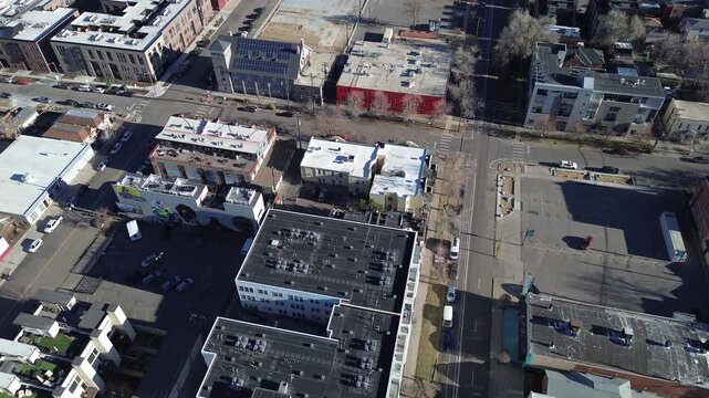 Building with bold mural anchors the block near 24th Street, surrounded by flat roofed structures and open lots. HVAC units, solar panels, angled shadows mark the urban composition, Denver, CO