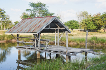 A wooden hut reflects in a calm pond under sunlight.
