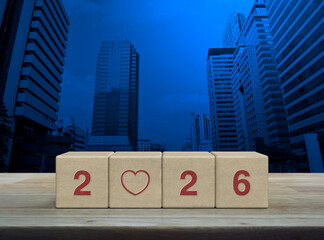 Love icon with 2026 letter on wood block cubes on wooden table over modern city tower and skyscraper, Happy new year and Valentines day 2026 concept