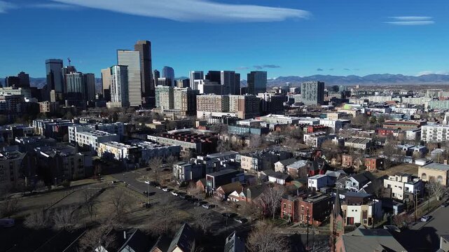 Residential blocks near Curtis Park feature brick homes, tree-lined streets winter, pointed church steeple. Mixed roof textures, layered skyline depth stretch toward the mountains, Denver, CO