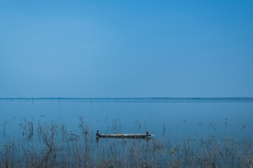 Fisherman on boat using net in morning sunshine at lake.