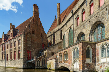 Naklejka premium Historic red brick and partly white houses on the canal embankment in the city of Bruges, Belgium The sky is cloudy blue