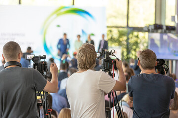 Press and media crew filming keynote speakers at business conference, professional event coverage, videographers recording corporate presentation