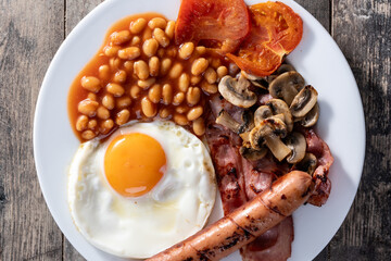 Full English breakfast with fried egg, bacon, sausages and beans on wooden table