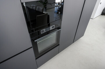 Modern kitchen with matte grey cabinetry, built-in black oven and microwave, sleek glass door, minimalist design, light grey floor, clean lines, contemporary aesthetic.