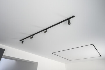 Modern ceiling with sleek black track lighting system; four adjustable spotlights, minimalist design, clean white surface, integrated square light panel.