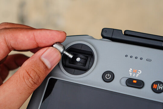 Close-up of a hand adjusting a small dial on the side of a modern drone controller with visible buttons and indicator lights showing operational status in a well-lit setting.