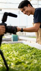 Young man in greenhouse filming fresh green produce
