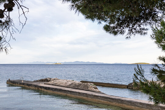 Quiet Seaside Pier With Calm Water, Distant Islands, Framed by Trees Under Sunlit Sky, Orebic, Croatia
