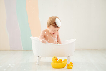 Naklejka premium a baby bathes in a tub with foam and rubber ducklings, the concept of child hygiene, a small child boy plays in a tub with foam or washes