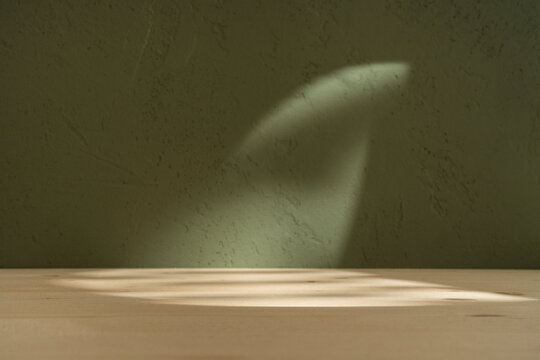 Wood table on boho green wall with sun light and shadows. Product cosmetic background.