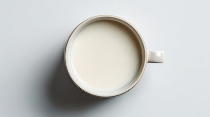 A white mug filled with milk sits on a plain white surface with a subtle shadow