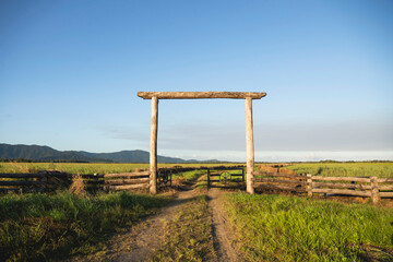 Rural landscape, farmland, featuring a wooden fence and gate with mountains in the background. On the road in between Daintree and Mossman, where the Daintree Rainforest meets the Great Barrier Reef i