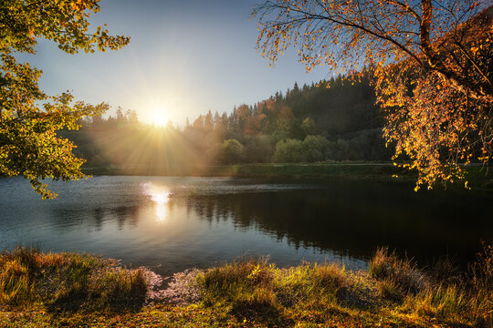 Golden sunset over a forest lake with bright sun rays and autumn foliage