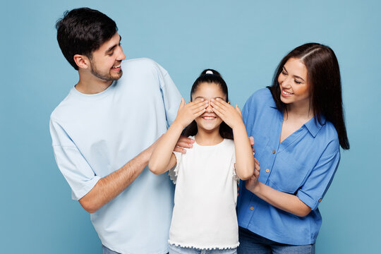 Young parent mom dad with child kid daughter girl wear casual clothes close eyes with hands play guess who or hide and seek isolated on plain blue background. Family day parenthood childhood concept..