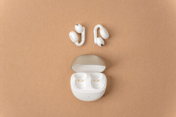 White wireless earbuds and open charging case on neutral beige background. Minimal modern audio technology flat lay, top view