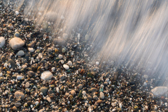 Long exposure of sea wave receding over colorful pebble beach