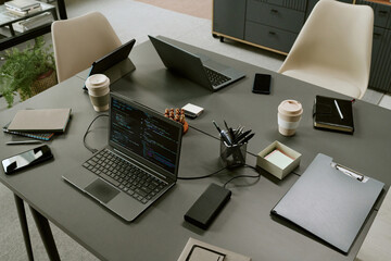 Modern office workspace featuring multiple laptops, tablets, smartphones, notebooks, coffee cups and clipboard arranged on desk, suggesting collaborative project or software development meeting