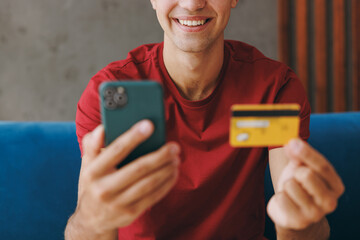 Cropped young man wears red t-shirt using mobile cell phone credit bank card shopping online order...