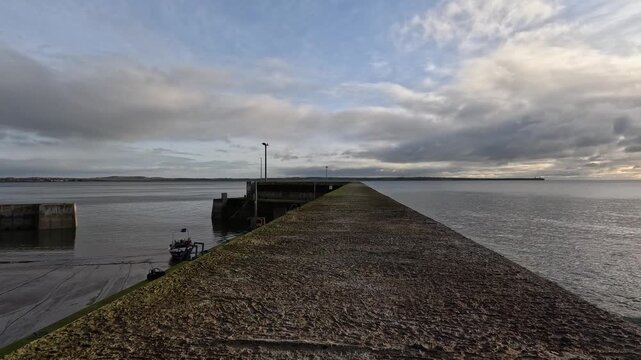 Low perspective view along concrete ocean pier as clouds drift overhead