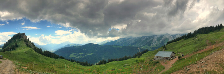 Panoramic view of alpine mountains, green valleys, and cloudy blue skies