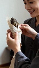 Woman carefully wraps small Buddha statue in textured paper and twine