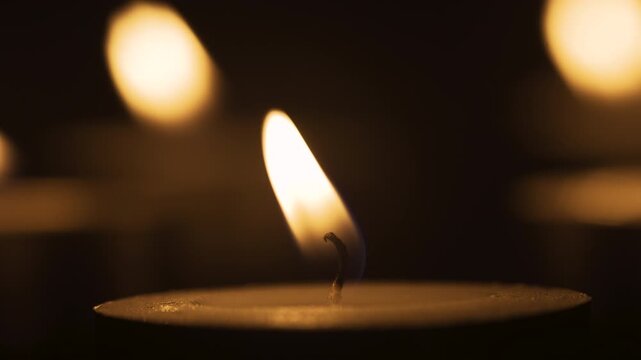 Macro DOF burning candle. Warm candlelight, flame and wick. Atmospheric glowing light on dark background