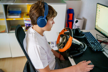 Teen boy playing racing video game with steering wheel at home.