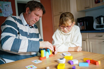 Obraz premium Little girl and her father playing wooden blocks parlor game at home.