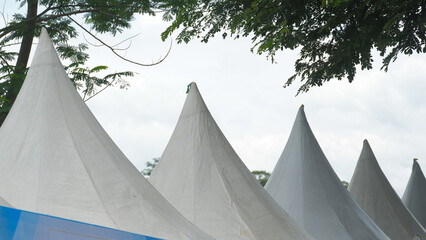 Row of White Conical Event Tents Under Green Trees Against Bright Sky