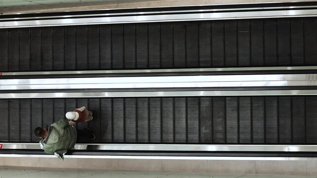 4K slow motion overhead view of people riding an escalator in a modern public space. Urban lifestyle, travel and daily commute concept with minimal design, symmetry and copy space.