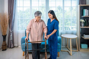 Obraz premium Senior elderly Asian woman using walker with caregiver support at home