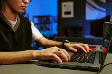 Young adult Caucasian man working on laptop computer in modern office setting, hands typing on keyboard, wearing smart watch, focused on screen, partial face visible