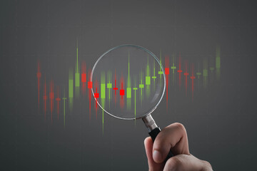 Hand holding magnifying glass analyzing stock market candlestick chart, representing financial analysis, trading strategy, investment research, market volatility, price movement data driven decision.