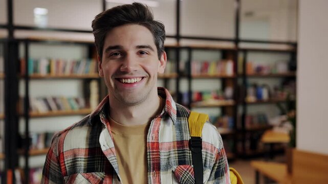 Young smart intelligent happy fun college student boy wears casual clothes backpack looking camera studying visit university library for learning new information choosing book. Knowledge concept