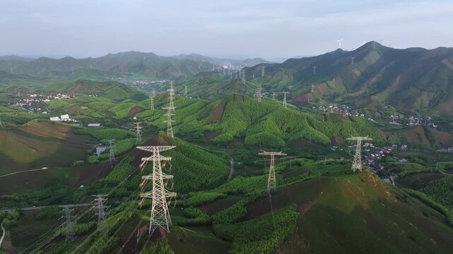Aerial view of high-voltage transmission towers standing among green rolling hills and terraced fields