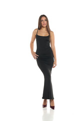 Fototapeta premium Studio shot of a woman with dark hair wearing a long black dress and high heels, standing with hands on hips, full body, on a white background