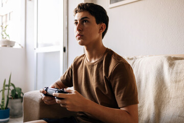 Teenager playing video game at home on sofa