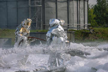 Firefighters are standing in foam at the fire. Firefighters in protective suits against high temperatures. Firefighters extinguish a fire at an oil refinery.
