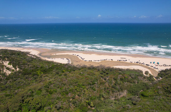 Aerial view of the shoreline where the dark green vegetation meets the bright white sand of 75 Mile Beach and the blue ocean waters, Eli Creek, K'Gari Fraser Island, Queensland, Australia.