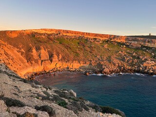 Rocky coastal cliffs illuminated by warm sunset light above calm blue sea, natural background for travel and nature concepts.