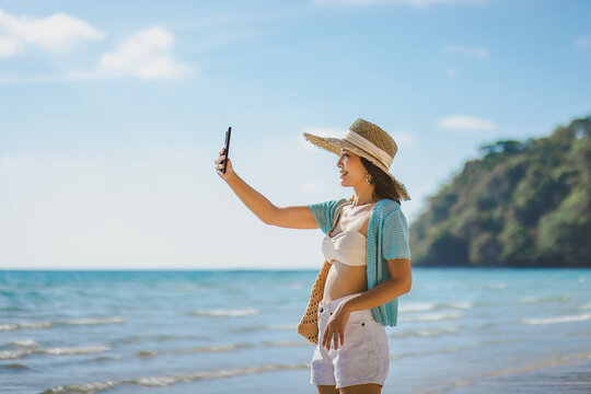 Happy asian traveler woman relax and use mobile phone for selfie on sea beach at day in Koh Kood Trat Thailand Travel summer holiday vacation concept