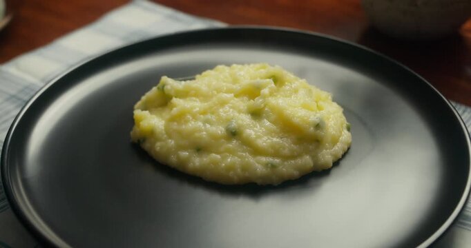 Chef plates a dish with creamy mashed potatoes and golden fried chicken drumsticks on a dark plate. Close-up of food plating process in a home kitchen, rustic style, natural light, homemade comfort